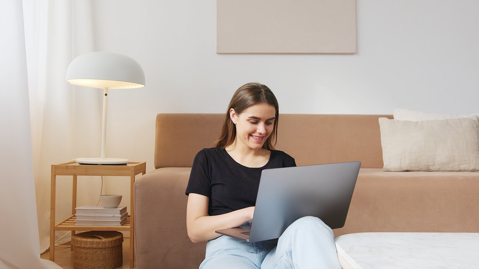 Cheerful woman typing on laptop on floor